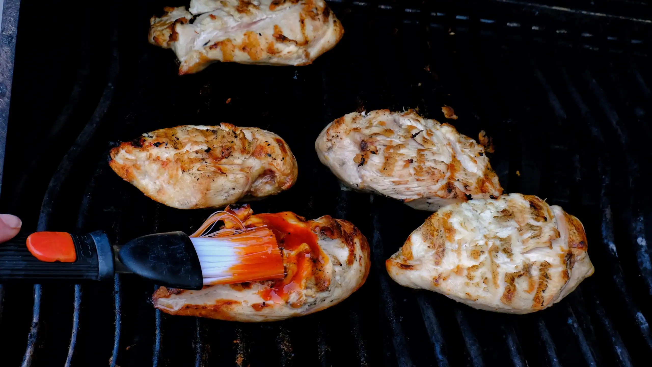 Juicy grilled chicken breasts being basted with barbecue sauce on a grill, showcasing outdoor cooking and barbecuing techniques.