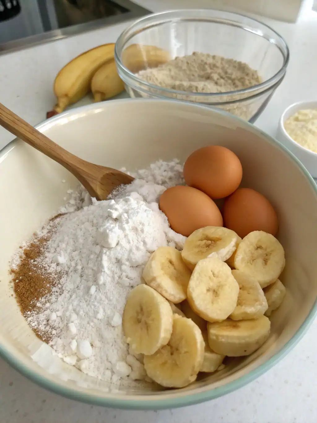 Flour, eggs, bananas, and baking ingredients for preparing banana bread or cake batter.