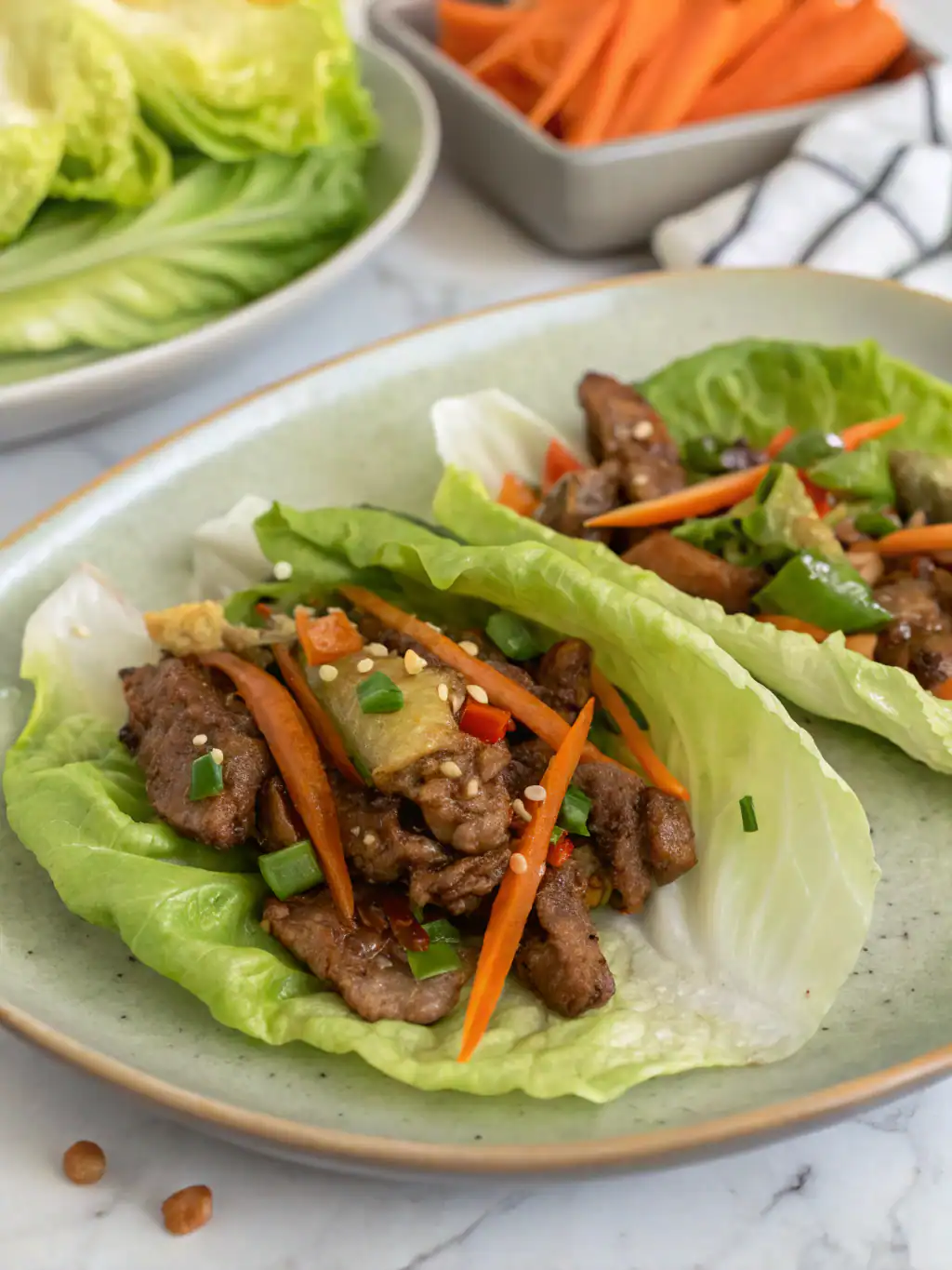 Sliced beef lettuce wraps with fresh vegetables and sesame seeds on a light green ceramic plate.
