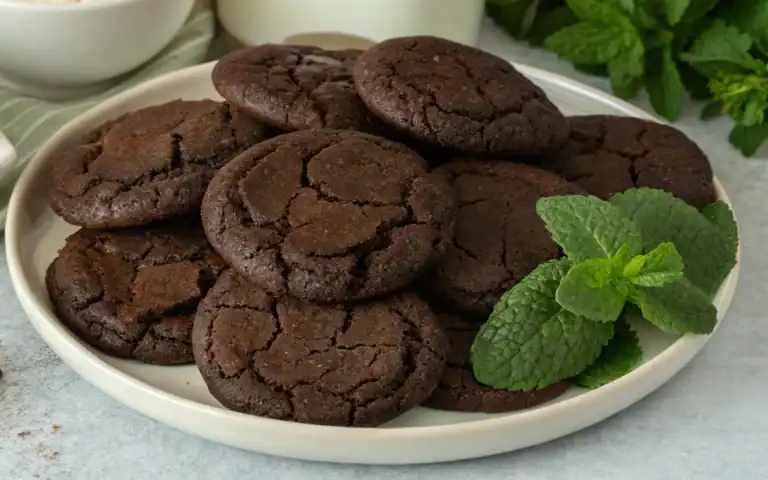 Rich chocolate cookies with eggs, chocolate pieces, flour, and mint leaves arranged on a white plate. Perfect for baking recipes and chocolate treats.
