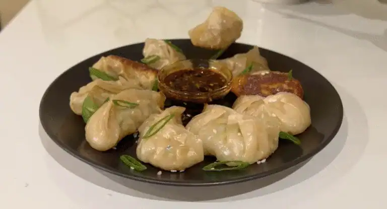 Steamed dumplings with dipping sauce on black plate, garnished with green onion slices, Asian cuisine, delicious hot dumplings for appetizer or main dish, appetizing food presentation.