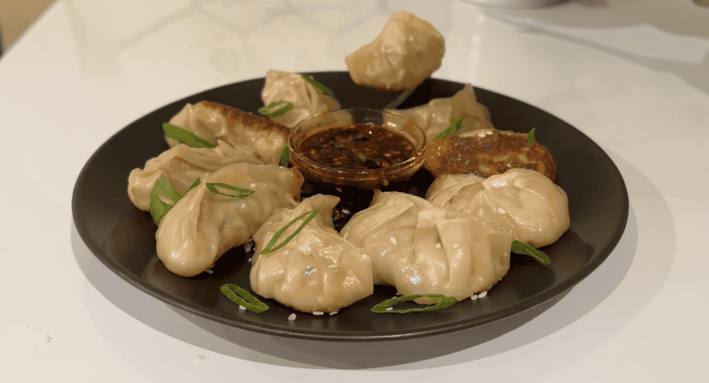 Steamed dumplings with dipping sauce on black plate, garnished with green onion slices, Asian cuisine, delicious hot dumplings for appetizer or main dish, appetizing food presentation.