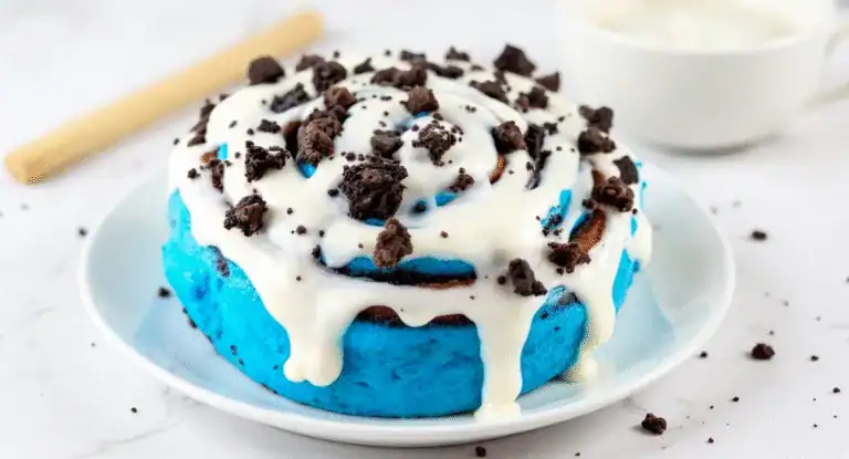 Creamy blue velvet cake with white frosting and chocolate cookie crumble topping on a white plate. Perfect for special occasions and celebrations.