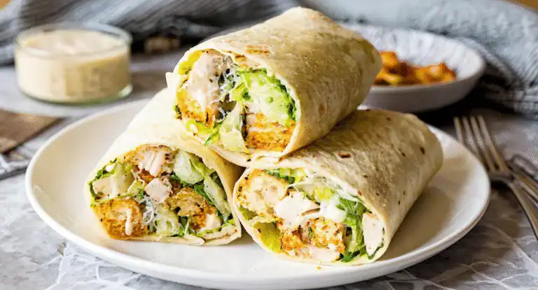 Fresh chicken Caesar wraps with crispy lettuce, creamy dressing, and grilled tortillas, served on a white plate for a delicious and healthy meal perfect for lunch or dinner.