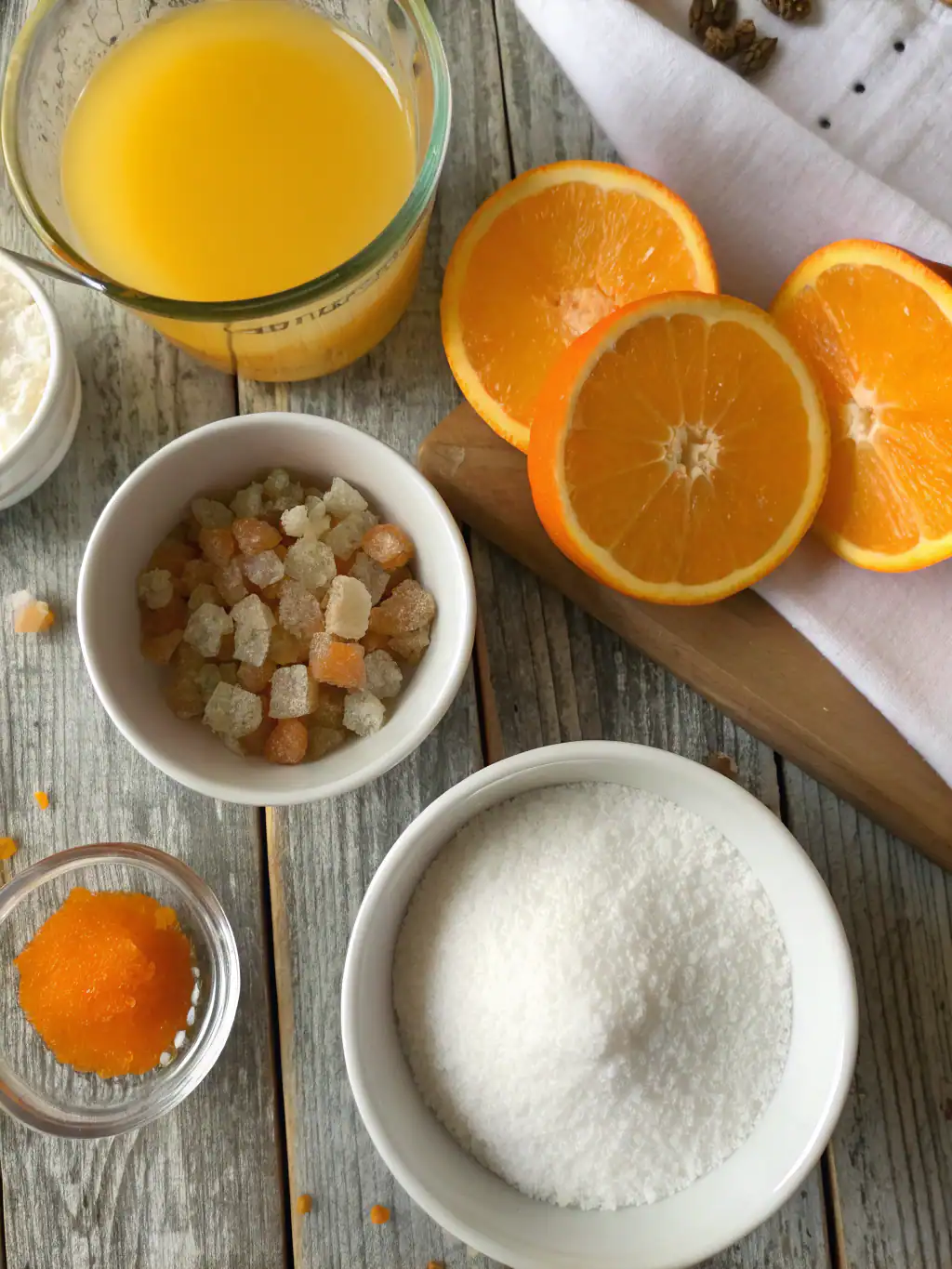 Fresh orange juice, sliced oranges, rock sugar, and other ingredients for orange syrup or dessert preparation on rustic wooden table.