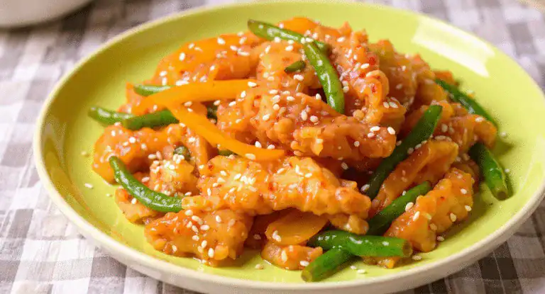 Crispy chicken stir-fry with bell peppers and green beans garnished with sesame seeds, served on a vibrant green plate, perfect for savory Asian-inspired meals.