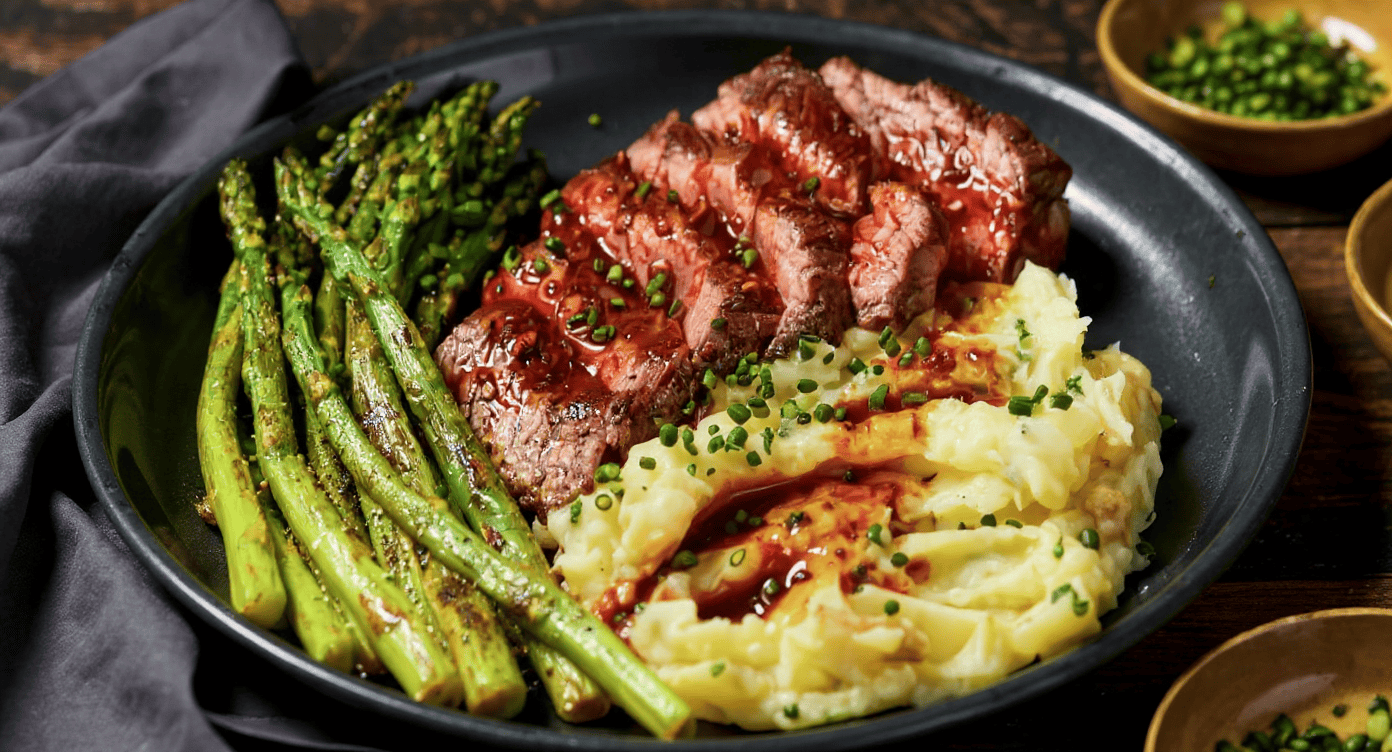 Juicy grilled steak served with roasted asparagus and creamy mashed potatoes garnished with chopped chives, perfect for meal prep and healthy eating.