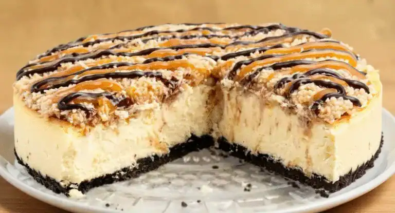 Creamy cheesecake with caramel, chocolate drizzle, and crumb topping, sliced to reveal a smooth, rich filling on a white plate. Perfect for dessert lovers and special occasions.