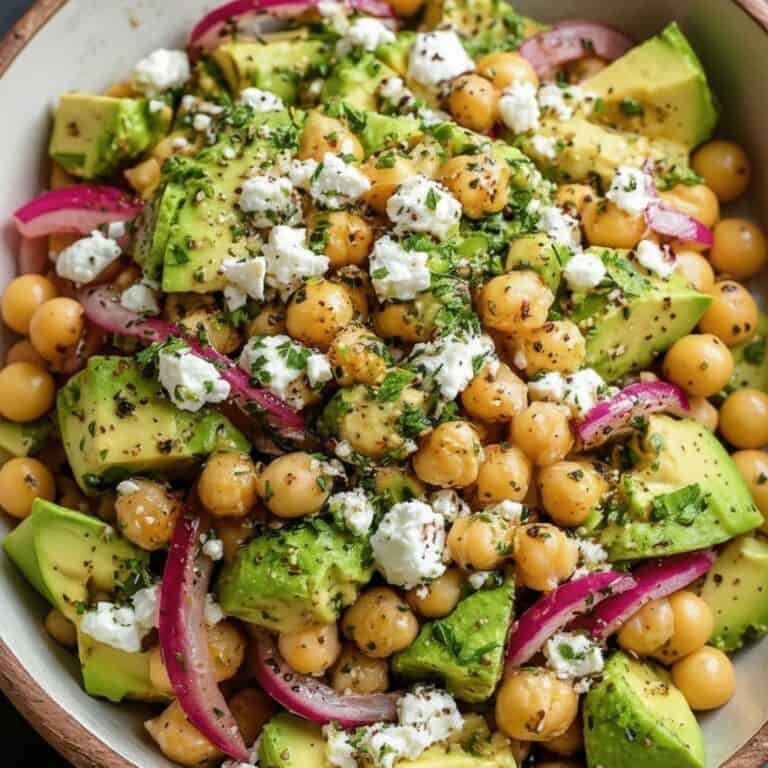 Fresh chickpea and avocado salad with crumbled feta cheese, sliced red onions, and chopped herbs in a rustic bowl. Healthy, vegan-friendly recipe ideal for nutritious meals or summer picnics.